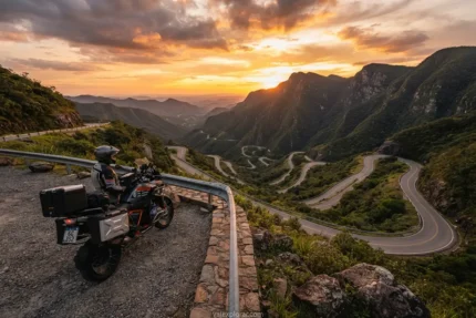 Roteiro de moto Serra do Rio do Rastro com uma motocicleta moderna estacionada em um mirante com vista para as curvas ao entardecer.